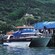 A catamaran tour boat docked at a pier with a group of Guests gathered near buildings and lush green hillside